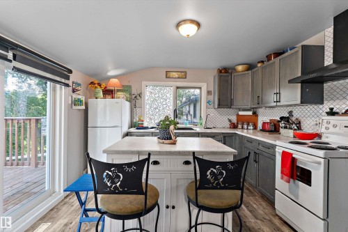 Kitchen featuring wood-finish flooring, a central island with countertop, gray cabinetry, white subway tile backsplash, and a sliding glass door to a deck - 5404 45 Avenue, Wetaskiwin, AB - Indoor Photo Showing Kitchen