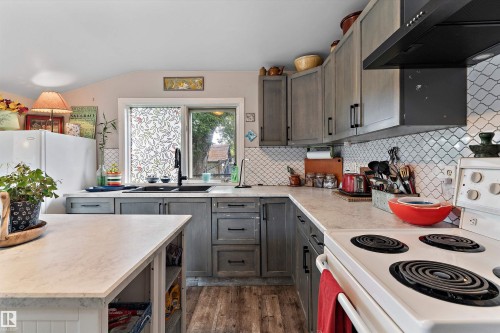 Kitchen featuring wood-finish flooring, gray cabinetry with dark hardware, a black sink, and white patterned tile backsplash - 5404 45 Avenue, Wetaskiwin, AB - Indoor Photo Showing Kitchen