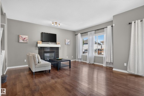 Wood-finish flooring, a fireplace with dark tile surround and white mantel, and multiple windows with white trim - 9515 221 Street Nw, Edmonton, AB - Indoor Photo Showing Living Room With Fireplace