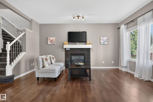 Hardwood-finish flooring, built-in fireplace with tile surround and white mantel, large windows, and a staircase with white balusters - 9515 221 Street Nw, Edmonton, AB - Indoor Photo Showing Living Room With Fireplace