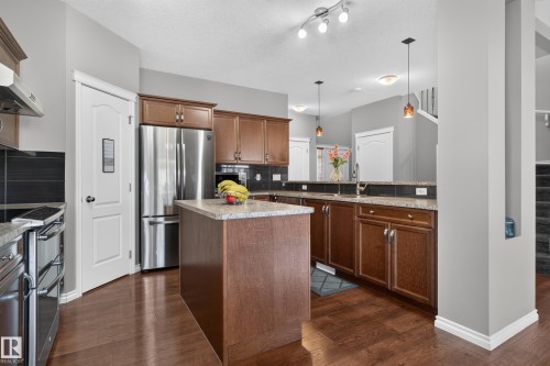 Wood-finish flooring with a kitchen island, stainless steel appliances, and dark wood cabinetry - 9515 221 Street Nw, Edmonton, AB - Indoor Photo Showing Kitchen With Double Sink With Upgraded Kitchen
