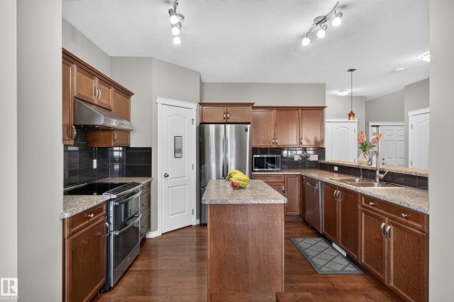 Kitchen featuring wood-finish cabinetry, stainless steel appliances, a center island with counter seating, and a dual-basin sink - 9515 221 Street Nw, Edmonton, AB - Indoor Photo Showing Kitchen With Double Sink