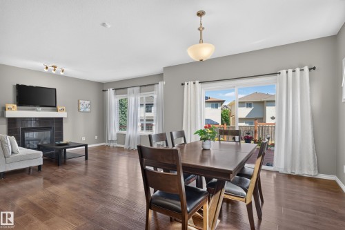 Spacious living area featuring wood-finish flooring, a tiled fireplace with white mantle, and large windows - 9515 221 Street Nw, Edmonton, AB - Indoor Photo Showing Dining Room With Fireplace