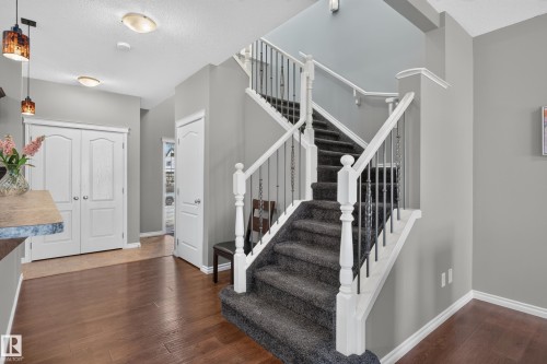 Carpeted staircase with white balusters and dark metal spindles, wood-finish flooring, two-panel white doors, and a stone-finish countertop - 9515 221 Street Nw, Edmonton, AB - Indoor Photo Showing Other Room