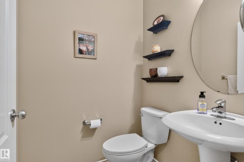 Pedestal sink with chrome faucet, circular wall mirror, and built-in wall shelving - 9515 221 Street Nw, Edmonton, AB - Indoor Photo Showing Bathroom