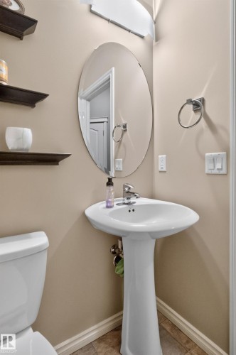 Pedestal sink with chrome faucet, oval frameless mirror, and wall-mounted shelving - 9515 221 Street Nw, Edmonton, AB - Indoor Photo Showing Bathroom