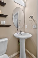Pedestal sink with chrome faucet, oval frameless mirror, and wall-mounted shelving - 