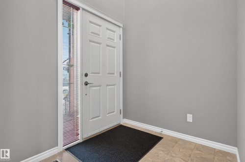 Welcoming entryway featuring a six-panel white entry door with sidelite window, dark-finish entry mat, wood-finish flooring, and neutral wall finishes throughout - 9515 221 Street Nw, Edmonton, AB - Indoor Photo Showing Other Room