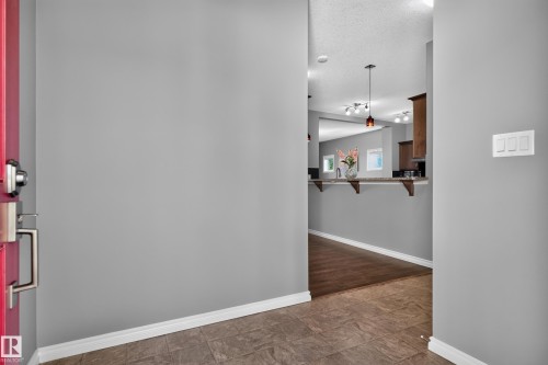 Red entry door with brushed nickel hardware, tile flooring, wood-finish flooring, and pass-through counter with pendant lighting - 9515 221 Street Nw, Edmonton, AB - Indoor Photo Showing Other Room
