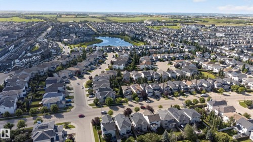 Aerial perspective showcasing a residential community with a central body of water, multiple homes with grey shingled roofs, and established streets - 9515 221 Street Nw, Edmonton, AB - Outdoor With View