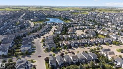Aerial perspective showcasing a residential community with a central body of water, multiple homes with grey shingled roofs, and established streets - 