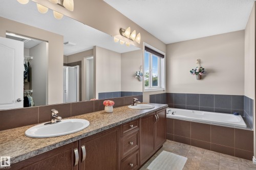 Dual vanity with granite-style countertop, integrated sinks, wood-finish cabinetry, built-in bathtub, and a window with blinds - 9515 221 Street Nw, Edmonton, AB - Indoor Photo Showing Bathroom