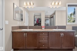 Double vanity with undermount sinks, stone-finish countertop, dark wood-finish cabinetry, and brushed nickel hardware - 
