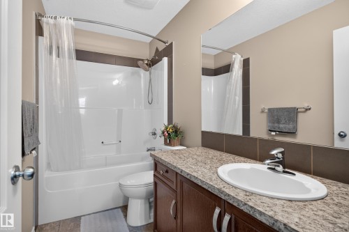 Bathroom featuring a built-in tub with shower, wood-finish vanity with an integrated sink, and a speckled countertop - 9515 221 Street Nw, Edmonton, AB - Indoor Photo Showing Bathroom