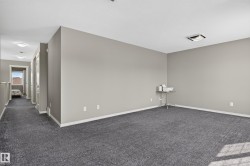 Spacious room with gray wall paint and dark gray carpeting, featuring a hallway with white trim and a window - 