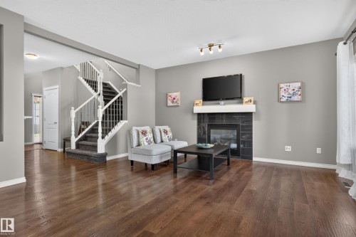Hardwood-finish flooring, a fireplace with a dark tile surround and white mantel, a staircase with white spindles, and light gray wall paint - 9515 221 Street Nw, Edmonton, AB - Indoor Photo Showing Living Room With Fireplace