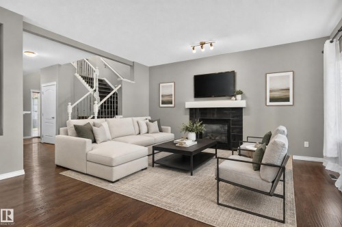 Wood-finish flooring, a fireplace with a tiled surround and mantel, a white spindle staircase, and recessed lighting - 9515 221 Street Nw, Edmonton, AB - Indoor Photo Showing Living Room With Fireplace