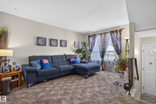 Wall-to-wall carpeting in a neutral tone, light-colored walls, and a white entrance door with an arched window - 18247 93 Avenue Nw, Edmonton, AB - Indoor Photo Showing Living Room