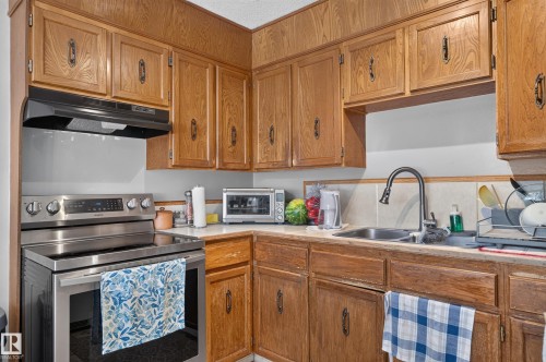 Wood-finish cabinetry with dark hardware, stainless steel range with overhead ventilation, and a stainless steel sink with a gooseneck faucet - 18247 93 Avenue Nw, Edmonton, AB - Indoor Photo Showing Kitchen With Double Sink