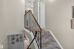 Carpeted staircase with a metal and wood-finish handrail, leading to an upper landing with a flush-mount light fixture - 