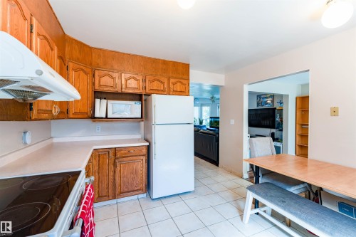 Kitchen featuring wood-finish cabinetry, white appliances, light-toned countertops, and tile flooring - 4609 38A Avenue Nw, Edmonton, AB - Indoor Photo Showing Kitchen