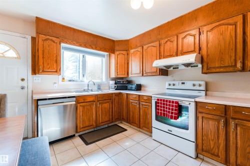 Kitchen with wood-finish cabinetry, white countertops, stainless steel dishwasher, and tile flooring - 4609 38A Avenue Nw, Edmonton, AB - Indoor Photo Showing Kitchen