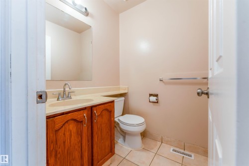 Wood-finish vanity with an integrated sink and light-toned countertop, mirrored wall, and tiled flooring - 4609 38A Avenue Nw, Edmonton, AB - Indoor Photo Showing Bathroom