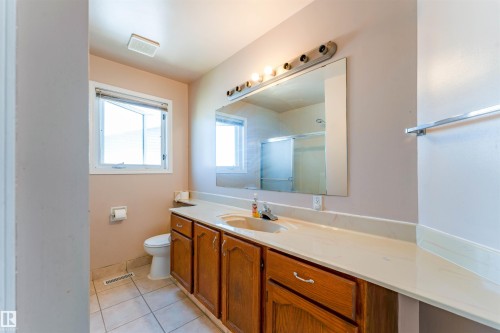 Wood-finish vanity cabinetry with a light-toned countertop, large wall-mounted mirror, and tile flooring - 4609 38A Avenue Nw, Edmonton, AB - Indoor Photo Showing Bathroom