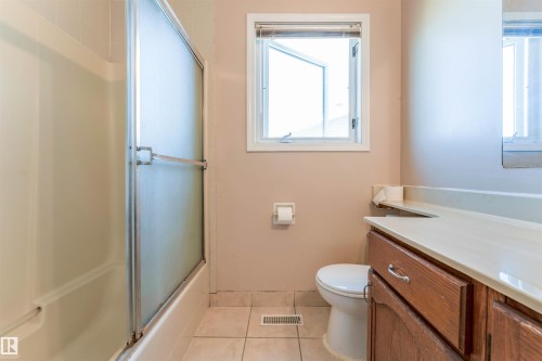 Wood-finish vanity with a light-toned countertop, tile flooring, and tub with a frosted glass enclosure - 4609 38A Avenue Nw, Edmonton, AB - Indoor Photo Showing Bathroom