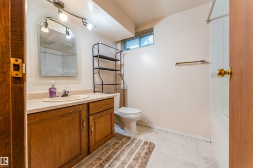 Wood-finish vanity with integrated sink, wall-mounted track lighting, and a white tiled shower surround - 4609 38A Avenue Nw, Edmonton, AB - Indoor Photo Showing Bathroom