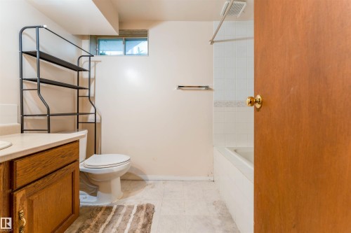 Bathroom featuring a wooden vanity with light-colored countertop, white toilet, and a bathtub with white tile surround - 4609 38A Avenue Nw, Edmonton, AB - Indoor Photo Showing Bathroom