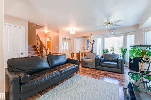Wood-finish flooring throughout, bay window with multiple panels, ceiling fan fixture, and a built-in staircase with wood railing - 4609 38A Avenue Nw, Edmonton, AB - Indoor Photo Showing Living Room
