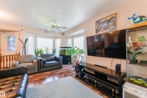 Wood-finish flooring, bay windows with vertical blinds, ceiling fan, and a built-in display cabinet - 4609 38A Avenue Nw, Edmonton, AB - Indoor Photo Showing Living Room