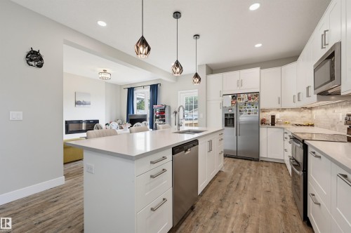 Contemporary kitchen featuring a large central island with seating, white shaker cabinetry, stainless steel appliances, and wood-finish flooring - 12219 93 Street Nw, Edmonton, AB - Indoor Photo Showing Kitchen With Stainless Steel Kitchen With Upgraded Kitchen