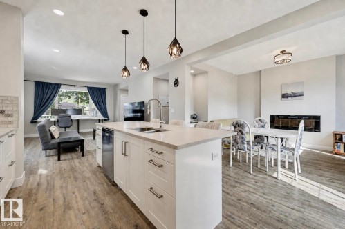 Open-concept living space featuring a central kitchen island with seating, a built-in fireplace, and wood-finish flooring - 12219 93 Street Nw, Edmonton, AB - Indoor Photo Showing Kitchen With Double Sink With Upgraded Kitchen