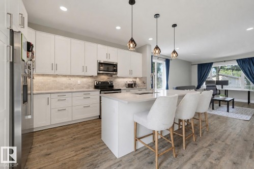 Open-concept kitchen featuring an island with pendant lighting, white cabinetry, integrated stainless steel appliances, and wood-finish flooring throughout - 12219 93 Street Nw, Edmonton, AB - Indoor Photo Showing Kitchen With Upgraded Kitchen