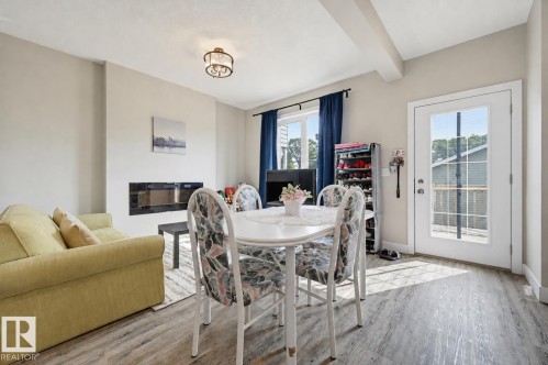 Open-concept living area featuring wood-finish flooring, a contemporary linear fireplace, and a glass-paneled exterior door - 12219 93 Street Nw, Edmonton, AB - Indoor Photo Showing Other Room With Fireplace