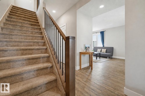 Staircase featuring neutral carpeted treads, dark wood-finish handrail, and black metal balusters - 12219 93 Street Nw, Edmonton, AB - Indoor Photo Showing Other Room