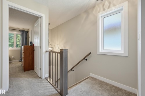 Carpeted hallway featuring a staircase with a wood-finish newel post and balusters - 12219 93 Street Nw, Edmonton, AB - Indoor Photo Showing Other Room