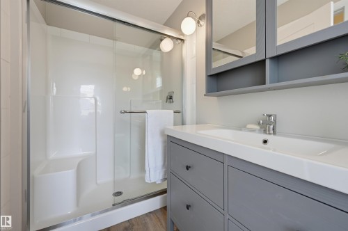 Bathroom featuring a glass-enclosed shower with integrated seating, gray wood-finish vanity with an integrated sink, chrome faucet, and mirrored medicine cabinet - 12219 93 Street Nw, Edmonton, AB - Indoor Photo Showing Bathroom