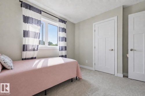 Interior room featuring light gray wall paint, light-colored carpet flooring, a white window frame, and two white paneled doors with brushed nickel hardware - 12219 93 Street Nw, Edmonton, AB - Indoor Photo Showing Bedroom