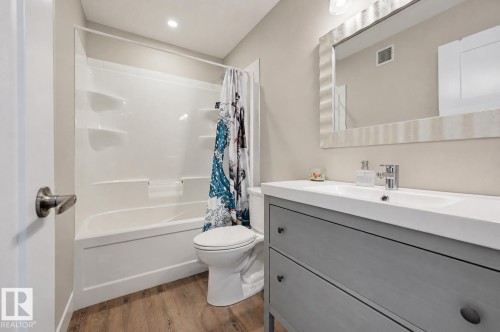 Bathroom featuring a white tub-shower combination, a gray vanity with integrated sink, wood-finish flooring, a contemporary framed mirror, and recessed lighting - 12219 93 Street Nw, Edmonton, AB - Indoor Photo Showing Bathroom
