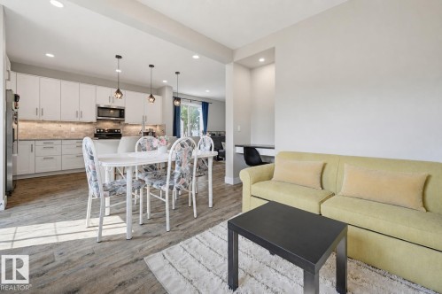 Bright open-concept living area featuring wood-finish flooring, a contemporary kitchen with white cabinetry and stainless steel appliances, and recessed lighting - 12219 93 Street Nw, Edmonton, AB - Indoor