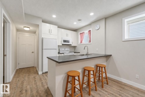 Kitchen featuring a breakfast bar with seating, white cabinetry, a double basin sink, and wood-finish flooring - 12219 93 Street Nw, Edmonton, AB - Indoor Photo Showing Kitchen
