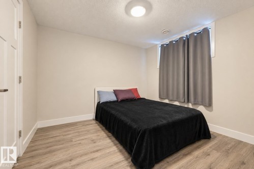 Room featuring wood-finish flooring, a window with trim, a solid panel door, and an overhead flush-mount light fixture - 12219 93 Street Nw, Edmonton, AB - Indoor Photo Showing Bedroom