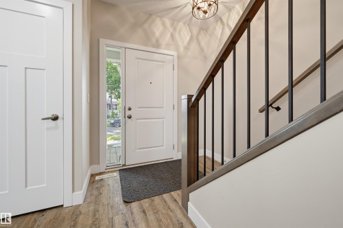 Foyer featuring wood-finish flooring, a white paneled entry door with a sidelight, and a staircase with dark wood-finish handrails and black metal balusters - 12219 93 Street Nw, Edmonton, AB - Indoor Photo Showing Other Room