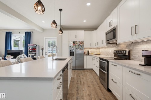 Kitchen featuring an expansive island with an undermount sink, pendant lighting, white cabinetry, stainless steel appliances, and wood-finish flooring - 12219 93 Street Nw, Edmonton, AB - Indoor Photo Showing Kitchen With Upgraded Kitchen