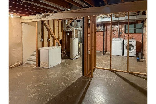 Unfinished basement space with exposed ceiling joists, concrete flooring, and built-in laundry appliances - 5511 92C Avenue Nw, Edmonton, AB - Indoor Photo Showing Basement
