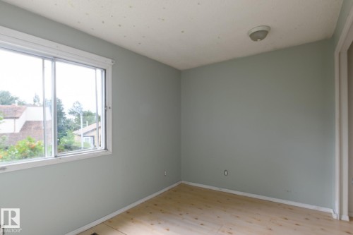 Light wood-finish flooring, light blue wall paint, white trim, and a white framed window - 5511 92C Avenue Nw, Edmonton, AB - Indoor Photo Showing Other Room