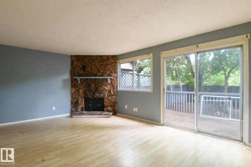 Stone-clad fireplace with mantel, wood-finish flooring, sliding glass door, and exterior wooden deck - 5511 92C Avenue Nw, Edmonton, AB - Indoor Photo Showing Living Room With Fireplace